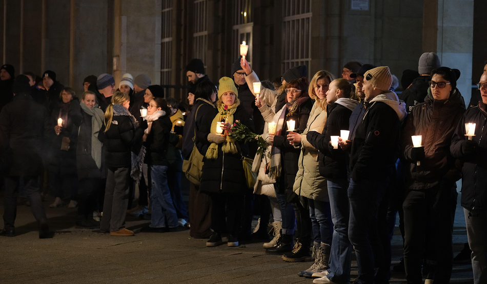 After dark, a semi circle of people dressed in winter clothes stand with candles, one of which is raised high. Credit: Sebastian Willnow/dpa/Alamy Live News 